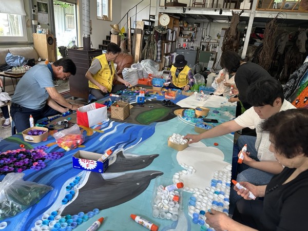 눈에 띄는 작품은 병뚜껑 2만 개로만 완성된 ‘성산일출봉을 품은 해녀’. 병뚜껑 하나하나의 색을 살려 제작된 이 작품은 도내 35개 기관과 주민들이 직접 병뚜껑을 모아 완성됐다.[사진=고의경 기획자]