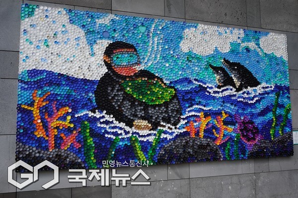 눈에 띄는 작품은 병뚜껑 2만 개로만 완성된 ‘성산일출봉을 품은 해녀’. 병뚜껑 하나하나의 색을 살려 제작된 이 작품은 도내 35개 기관과 주민들이 직접 병뚜껑을 모아 완성됐다.[사진=고의경 기획자]